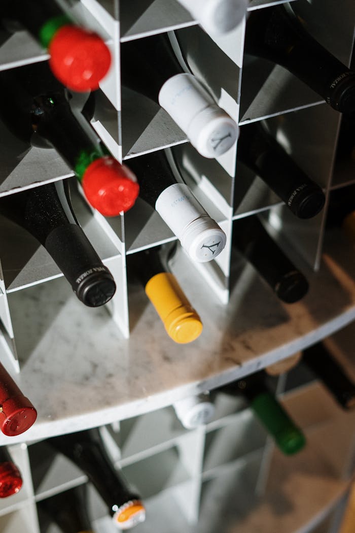 Accueil - Guide Cave à Vin Various wine bottles stored in a geometric wine rack, offering a close-up of bottle tops with a mix of colors.