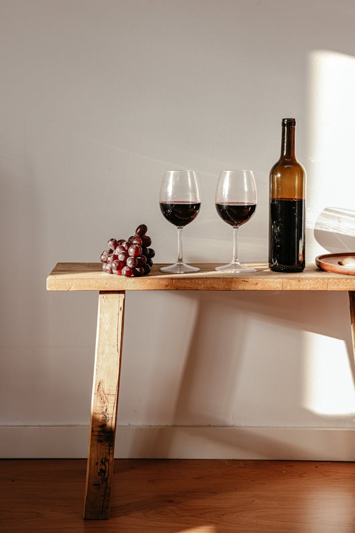 Accueil - Guide Cave à Vin Sophisticated wine setting with glasses and a bottle on a wooden table, bathed in natural light.